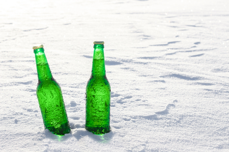 Two bottles of cold beer on the snow at sunset. Close up view.の写真素材