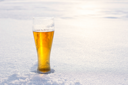 Mug of cold beer in the snow at sunset. Beautiful winter background. Outdoor recreation. Advertising of alcoholic beverage. Booze and holidays.の写真素材