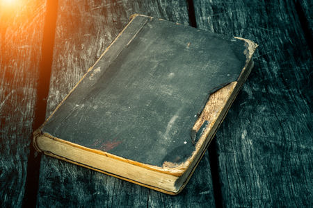 Old tattered book on a wooden table. Reading by candlelight. Vintage composition. Ancient library. Antique literature. Fabulous atmosphere. Medieval and mystical background, vintage style, religion.の写真素材