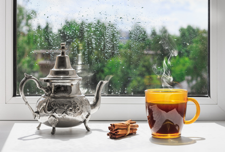 Cup of hot coffee on the windowsill. Outside the window the rain. Rainy weather behind the window.の写真素材