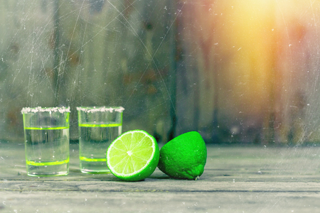 Shot glasses with golden mexican tequila with lime slices and salt on old wooden table. Selective focus. Traditional Mexican drink. Alcoholic beverage. Close up with copy space. Vintage design.の写真素材