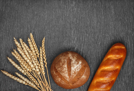 Ears of wheat, freshly baked bread and a loaf on wooden background.の写真素材