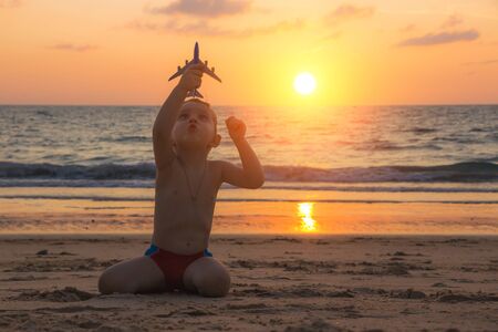 Little baby boy is playing with toy plane on the sand of amazing tropical beach of Andaman sea in Thailand at sunset. Concept of travel by plane with children. Family holidays.の写真素材