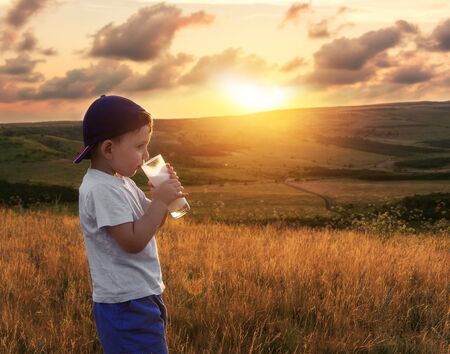 Happy childhood. Cheerful kid is drinking milk at the nature. Scenic view of the meadows and hills.の写真素材