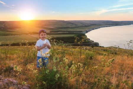 Happy childhood. Cheerful kid is drinking milk at the nature. Scenic view of the meadows, hills and the sea.の写真素材