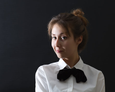 Portrait of an attractive beautiful happy young caucasian business woman / lady / girl / female / model  dressed in a office suit (white blouse and black bow-tie) and smiling on dark  background with empty copy space.の写真素材