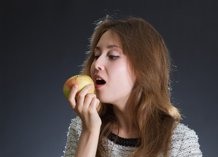 Portrait of an attractive beautiful young caucasian woman / lady / girl / female / model eating an apple on dark background with empty copy space.の写真素材