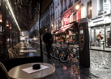 Narrow Paris street near the city center at the rainy autumn evening. Empty cafe, bicicles for rent and little shops are visible.のeditorial素材