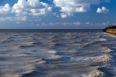 Landscape of the Sea of Azov by a windy summer evening. Waves on the water surface, blue sky with clouds, high coast.の写真素材