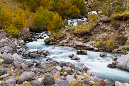 Mountain stream by an autumn surrounded by trees with yellow foliage and stones.の写真素材