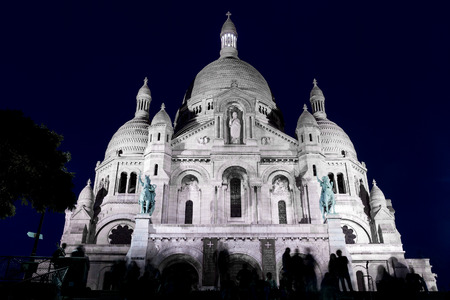 The Basilica of the Sacred Heart of Paris (Basilique du Sacre Coeur, Paris) by an evening with a dark blue sky as a background and with people silhouettes in front of itの写真素材