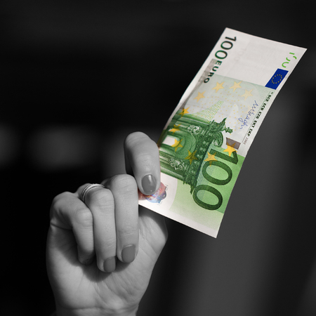 Black and white woman's hand holding (showing) colorful 100 Euro banknoteの写真素材
