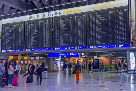 Interior of the terminal T1 in international Frankfurt Airport, Frankfurt am Main, Germany. Time table with inscription 'Boarding. Flying. Smiling.', people passengers with luggage and airport interior. November 8, 2014.のeditorial素材