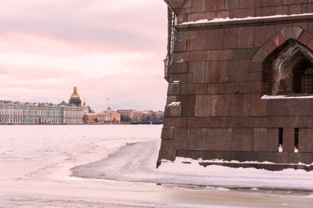 Landmark in Saint Petersburg, Russia: the Peter and Paul fortress wall by a winter day, the Neva river covered by ice and snow, sky with clouds and historical center of the city as a background.の写真素材