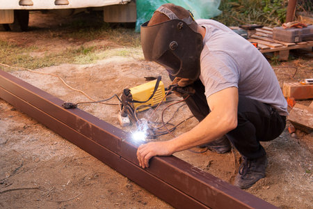The welder welds square pipes that lie on the ground