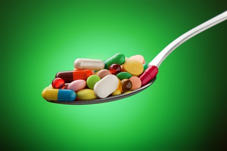 Various pills, capsules and tablets stacked on a spoon on a green backgroundの写真素材