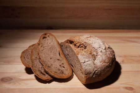 Fresh handmade wheat bread cut into pieces on wooden background in the contrast light. horizontal...