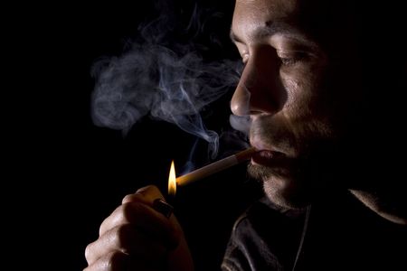 Young man lighting a cigarette on black backgroundの写真素材