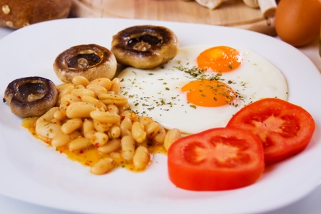 Fried eggs with beans, mushrooms and tomato served for healthy breakfast (focus on eggs)の写真素材