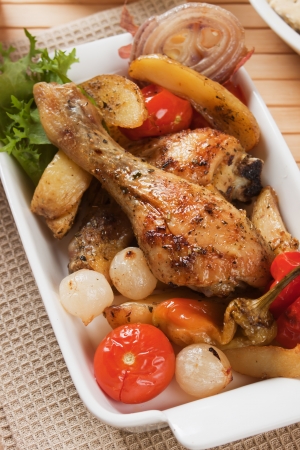 Roasted chicken leg with potatoes, onion and tomatoの写真素材