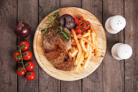 Beef rib-eye steak with french fries on wooden boardの写真素材