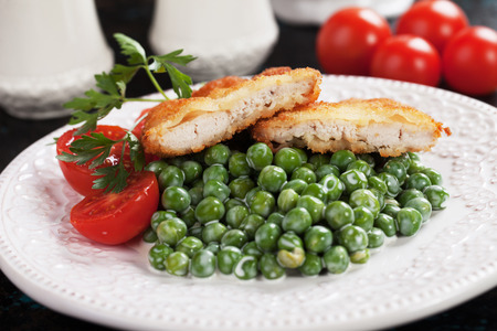Breaded chicken steak served over cooked green peasの写真素材