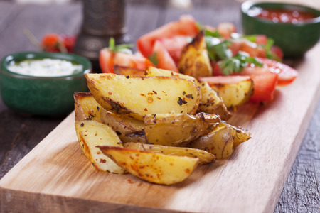 Spicy oven roasted potato wedges with tomato saladの写真素材