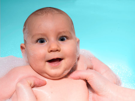 Little cute baby is bathed in water in foam