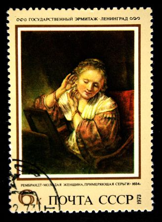 A stamp prunted in the USSR shows paint "Young woman trying earrings" by artist Rembrandt, stamp from collection Hermitage, circa 1973のeditorial素材
