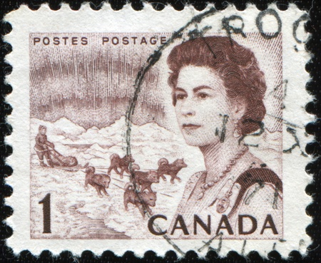 CANADA - CIRCA 1971: A post stamp printed in Canada shows Portrait of Elizabeth 2 on the background of male control dog team, circa 1971のeditorial素材