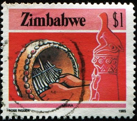 ZIMBABWE - CIRCA 1985: A stamp printed in Zimbabwe shows Playing Mbira (musical instrument) at the right Zimbabwe Bird soapstone sculpture, circa 1985の写真素材