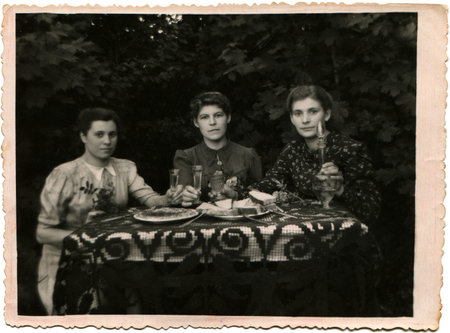 Soviet Union - circa 1952 Three young women holding glasses of alcohol, sitting at a table covered...