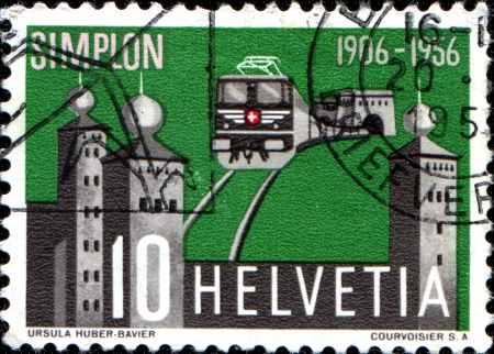 SWITZERLAND - CIRCA 1956  A stamp printed in Switzerland issued for the 50th anniversary of opening of Simplon Tunnel shows electric train emerging from the tunnel and Stockalper Palace, circa 1956のeditorial素材