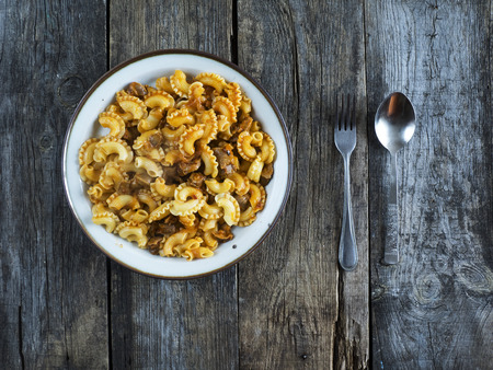 Pasta with meat, stewed in tomato sauce on a plate on old weathered wooden tableの写真素材