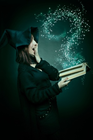 Pretty witch with magic book posing over dark background.の写真素材