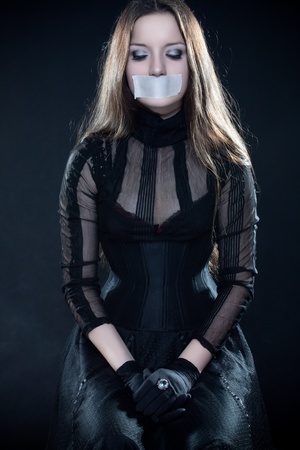 Pretty gothic girl in corset with sealed mouth looking downの写真素材