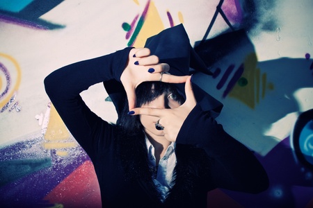 Pretty young witch in hat posing over wall with graffitiの写真素材