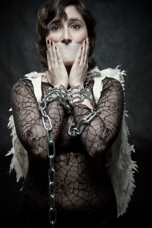 Pretty angel with sealed mouth and bounded hands posing ovre dark backgroundの写真素材