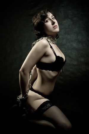 Pretty girl bounded by chains sitting on the floor over dark backgroundの写真素材