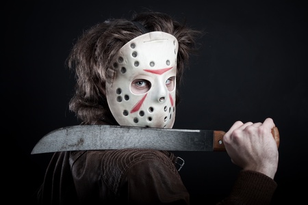 horrible maniac in mask with machete posing over dark backgroundの写真素材