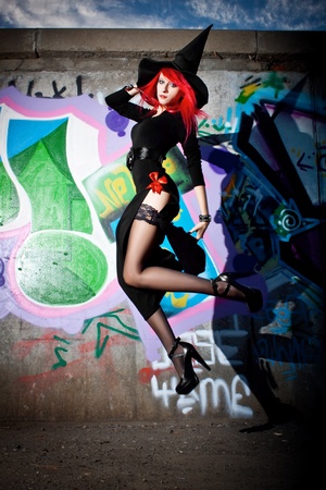 Pretty sexy redhead witch jumping over wall with graffiti