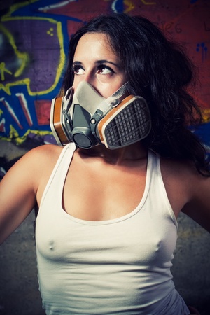 Pretty young girl in respirator posing over wall with graffitiの写真素材
