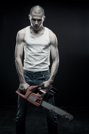 Young strong guy with chainsaw posing over dark backgroundの写真素材