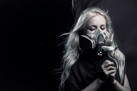 Pretty girl in gas mask holding flower in her handsの写真素材