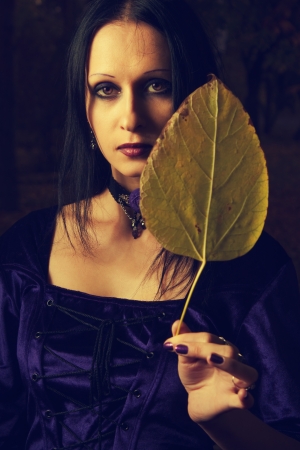 Portrait of pretty gothic girl in purple dress with a yellow leaveの写真素材