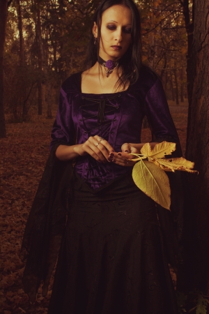 Portrait of pretty gothic girl with leaves standing in the autumn forestの写真素材
