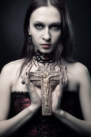 seductive young woman in red corset holding crucifix over dark backgroundの写真素材