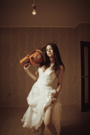 Pretty sexy bride with bloody chainsaw in empty roomの写真素材