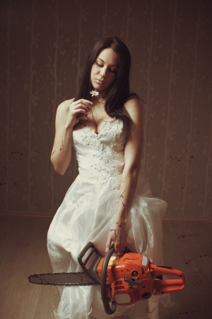 Pretty sexy bride posing with bloody chansaw and camomile in empty roomの写真素材