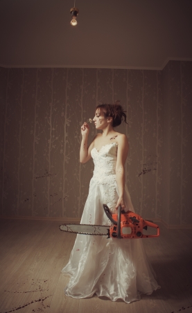 Pretty bride with bloody chainsaw and chamomile in empty roomの写真素材